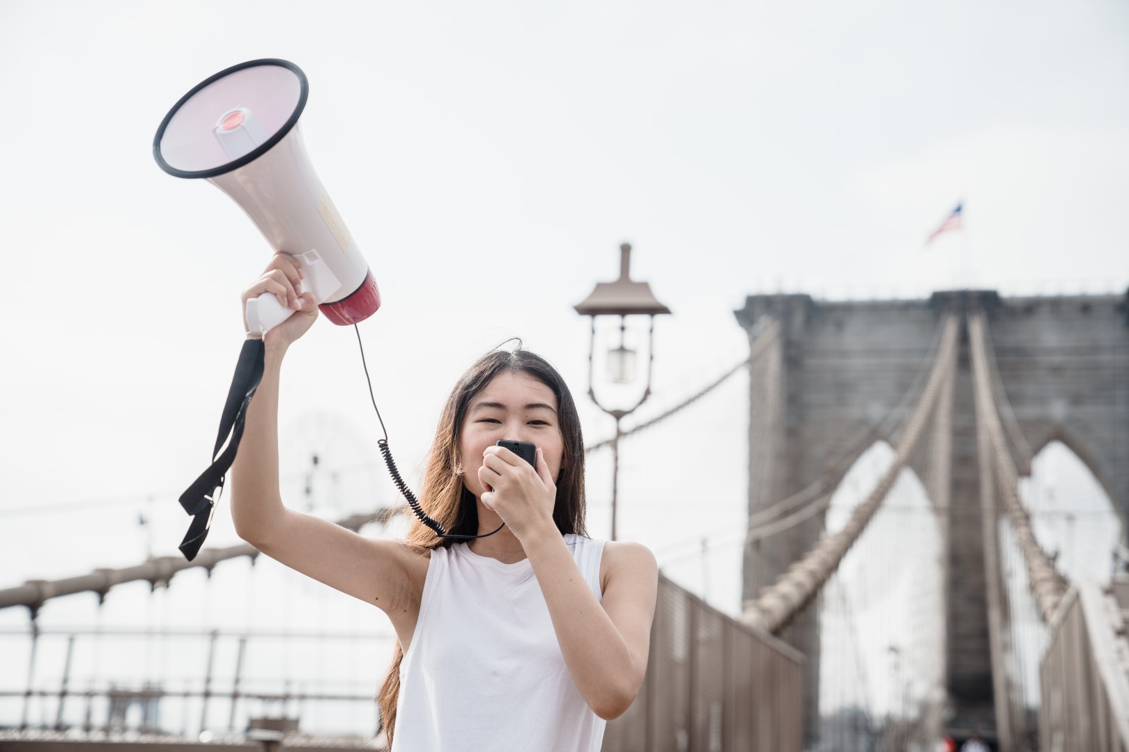 A woman holding up a megaphone while standing on the side of a bridge.