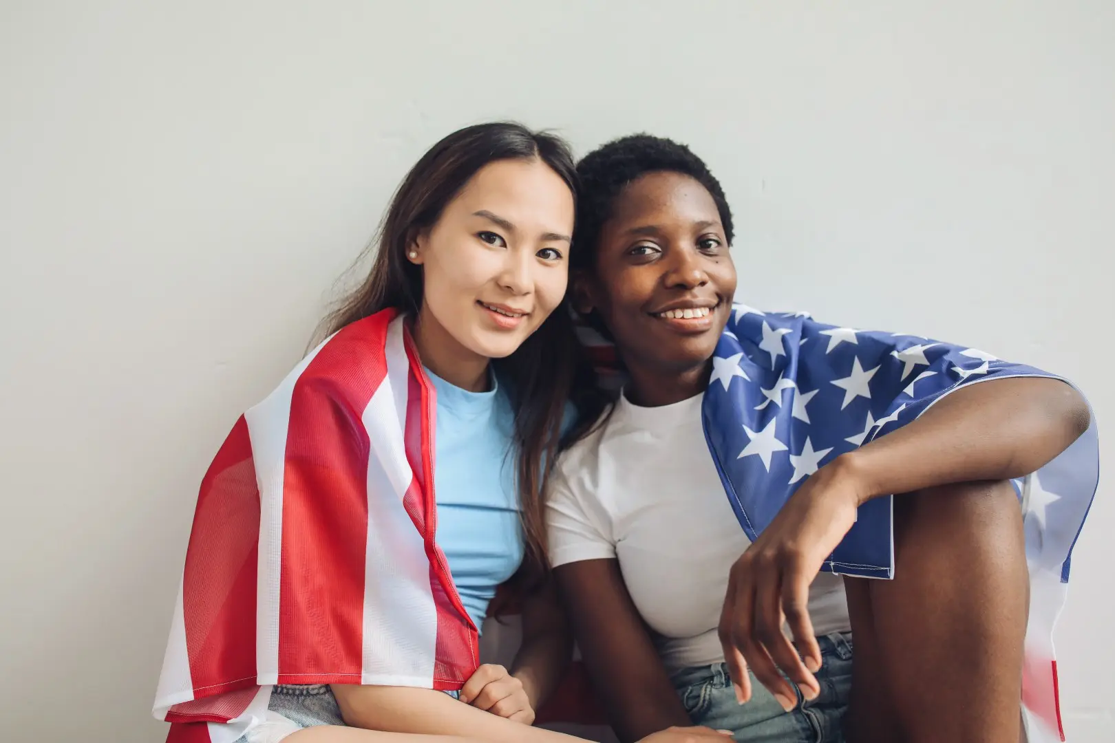 Two young women sitting on a couch wrapped in american flags.